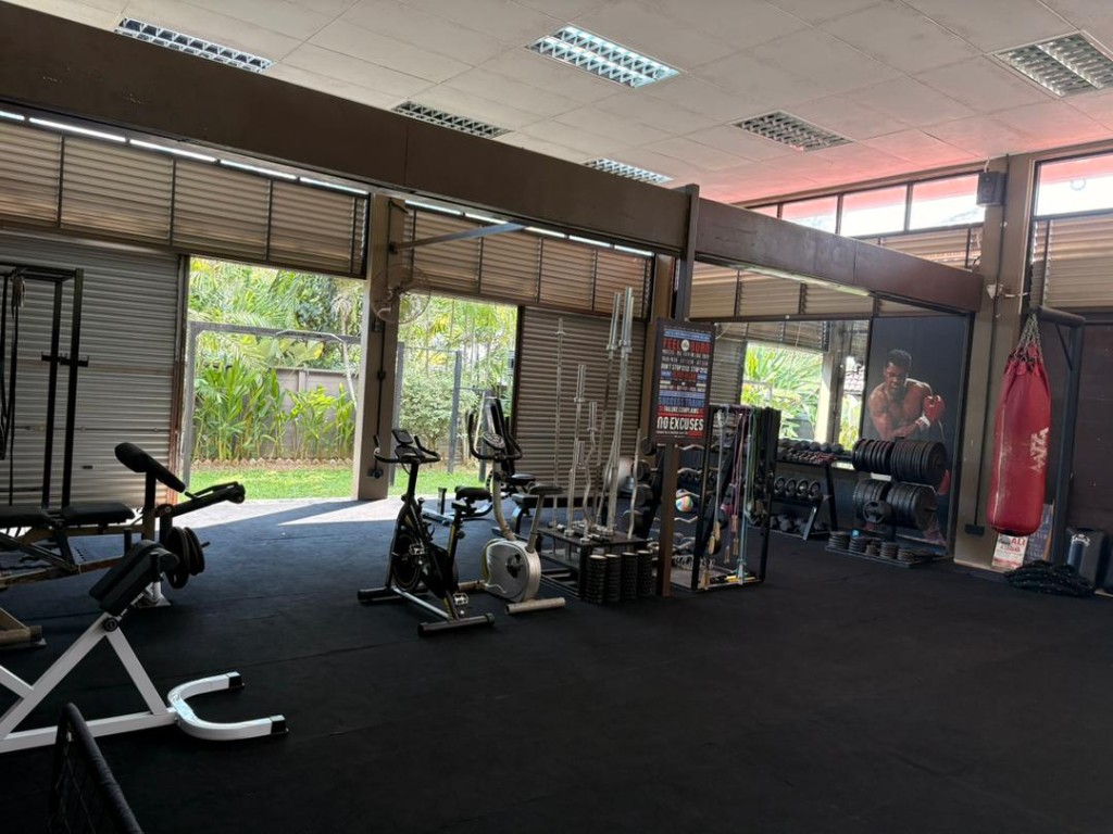 Wide view of the open-bay Bambu gym with bench, spin bikes, weight rack, and Muhammad Ali mural