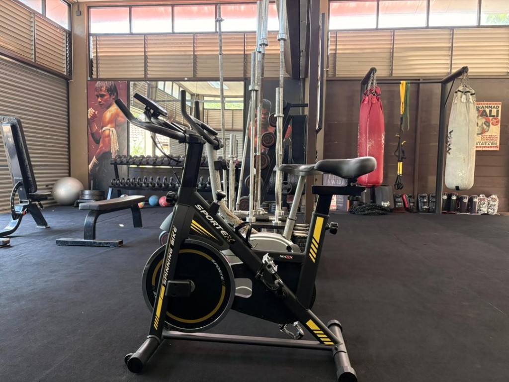 Spin bike on the gym floor with heavy bags and Muay Thai mural in the background at Bambu